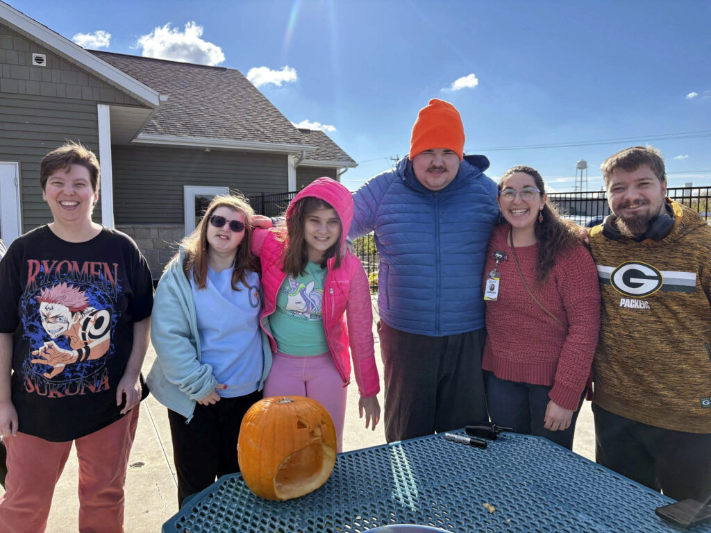 Five Onward Adult Day Center participants and one staff member posing outside with a pumpkin.