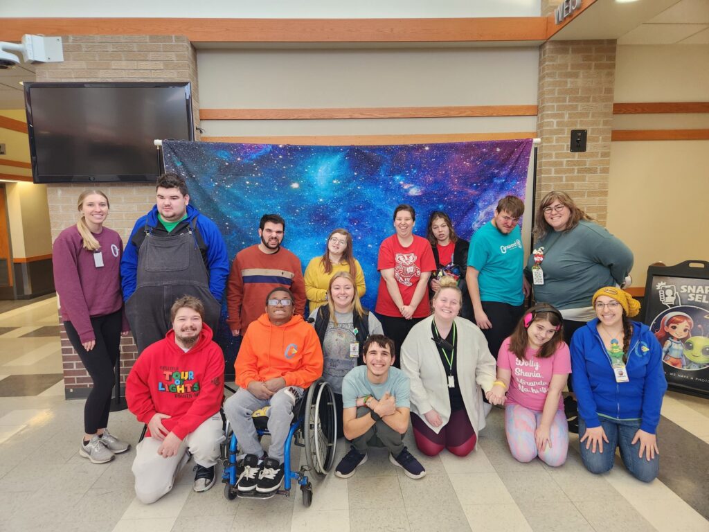 Group photo of Onward Adult Day Center participants and staff, in front of a galaxy banner.